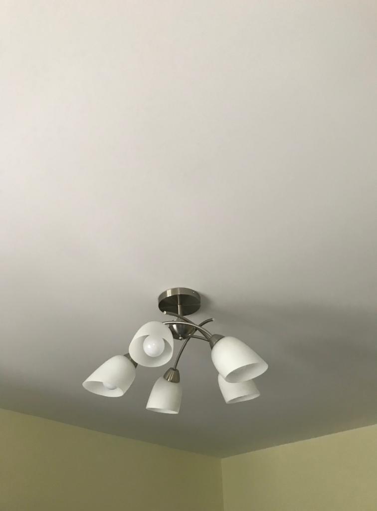 Lampa sufitowa z pięcioma białymi kloszami i żarówką LED w jednym z kloszy, zamontowana na suficie w mieszkaniu w Poznaniu.