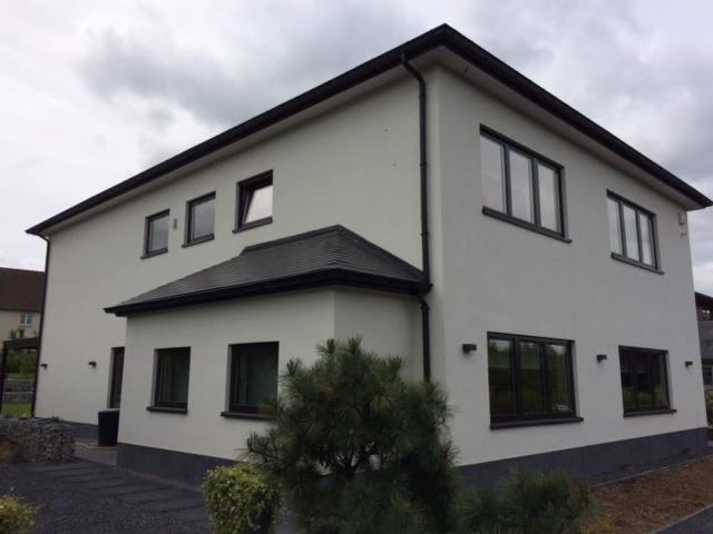 Dwukondygnacyjny dom z jasną elewacją i ciemnymi ramami okiennymi, widok z zewnątrz w pochmurny dzień.