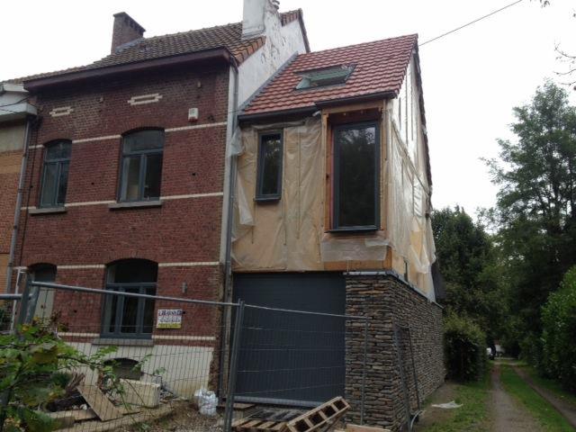 Dom w trakcie prac elewacyjnych, zabezpieczony folią, z widocznym fragmentem elewacji z kamienia i starą ceglaną częścią budynku.