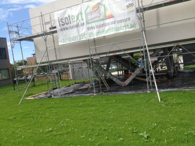 Budynek w trakcie prac z rusztowaniem, widoczna baner reklamowy firmy Isolext i częściowo ocieplona ściana.