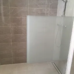 Kabina prysznicowa typu walk-in z szarymi płytkami imitującymi marmur na ścianach i podłodze, chromowana bateria i deszczownica, oraz odpływ liniowy w podłodze.