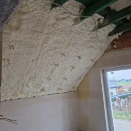 Poddasze ocieplone pianką poliuretanową, widoczne krokwie i szyny montażowe, surowy stan wykończenia ścian.