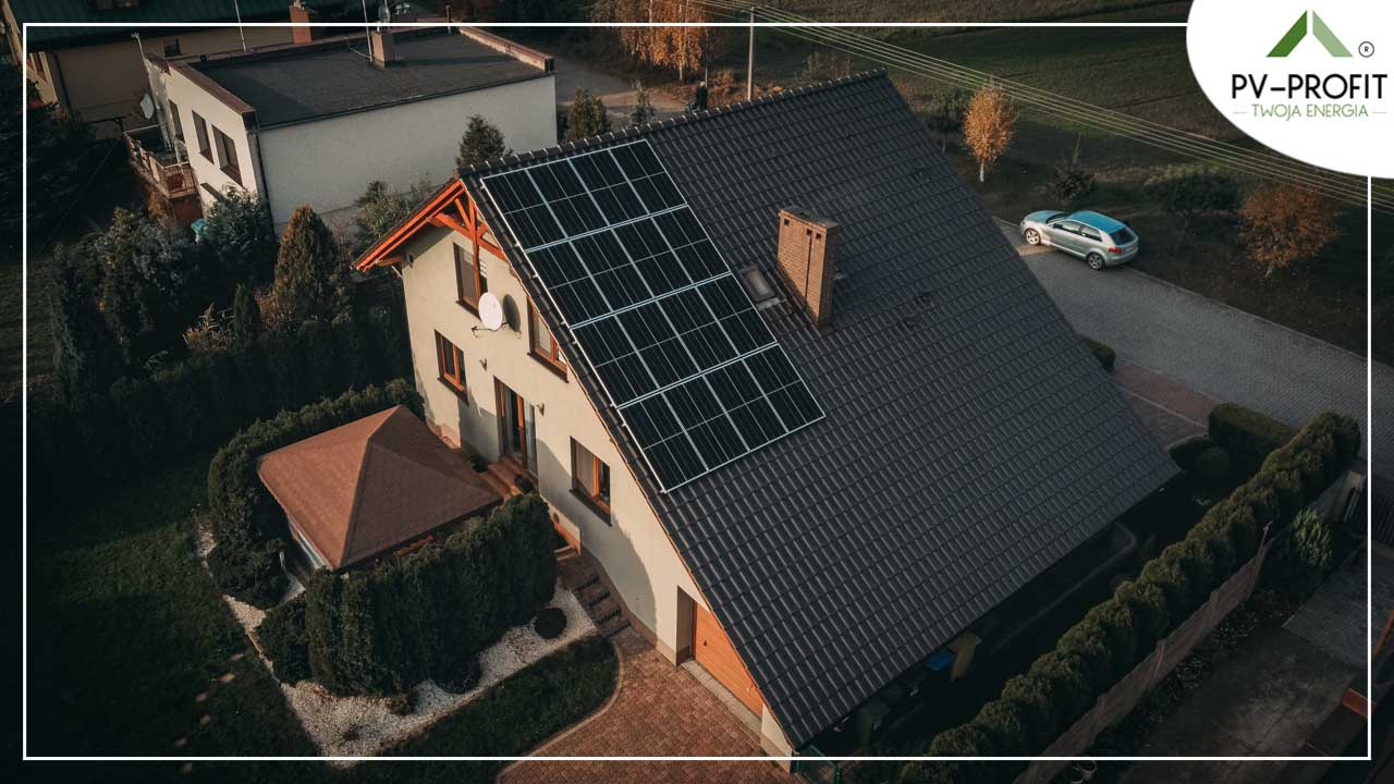 Dom jednorodzinny z panelami słonecznymi na dachu, widok z góry, obok zaparkowany samochód osobowy.