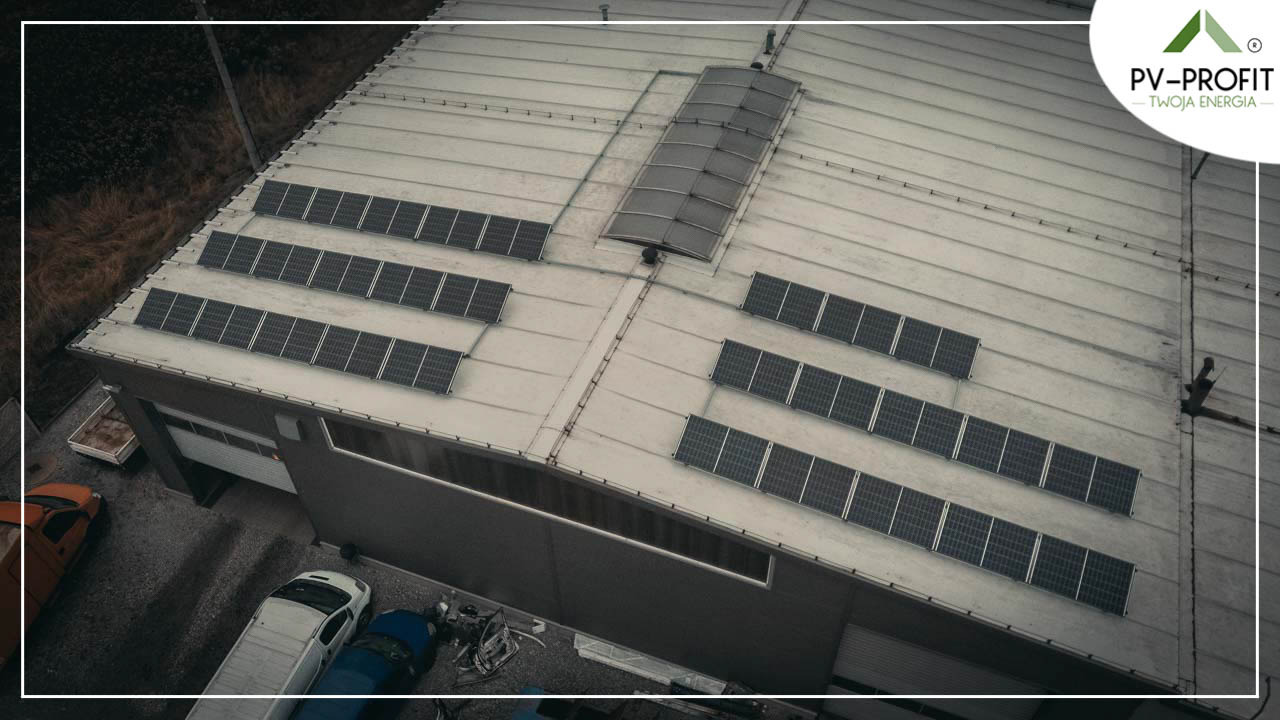 Widok z góry na dach budynku przemysłowego z zainstalowanymi panelami słonecznymi ułożonymi w rzędach, logo firmy PV-PROFIT w prawym górnym rogu.