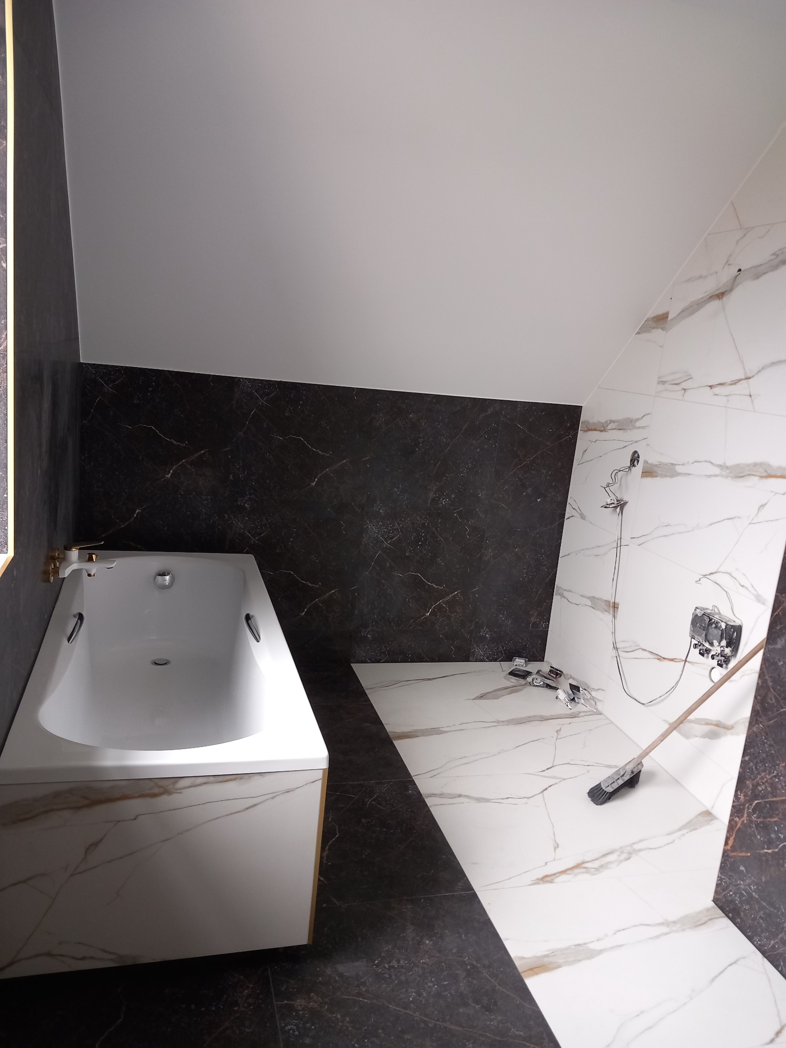 Nowoczesna łazienka w Brzesku w trakcie wykańczania, widoczna wanna z marmurowym wykończeniem, ściany wyłożone płytkami imitującymi marmur, na podłodze pozostałości po pracach i narzędzia glazurnicze.
