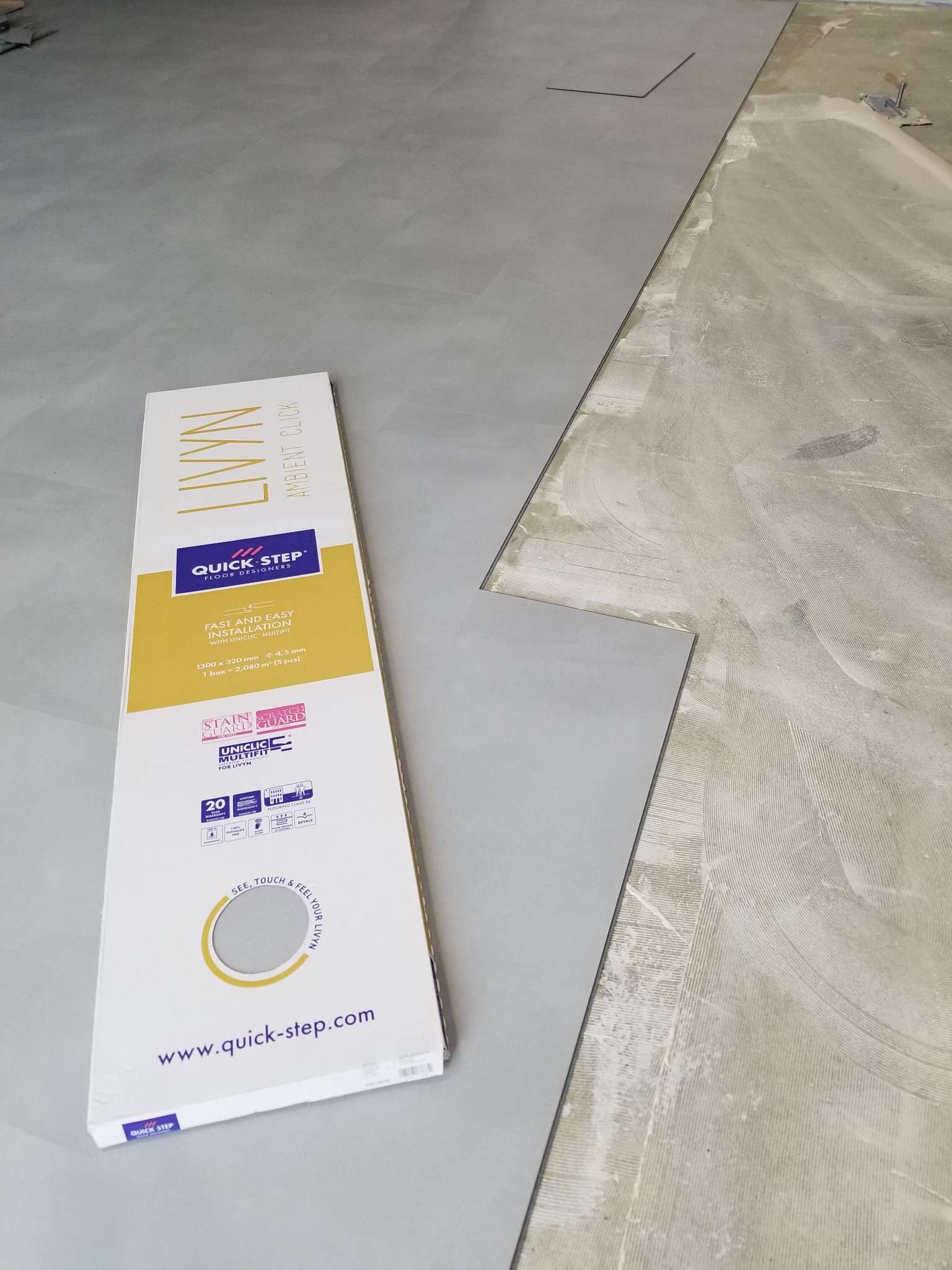 Paczka paneli podłogowych Quick-Step Livyn Ambient Click leży obok częściowo ułożonej podłogi we Wrocławiu, widoczne ślady kleju na podłożu.