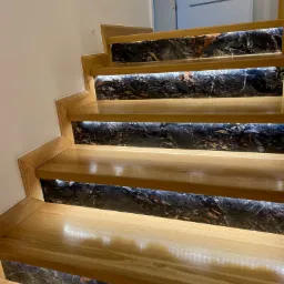 Drewniane schody z marmurowymi podstopnicami i subtelnym podświetleniem LED, widok z dołu, nowoczesny design.