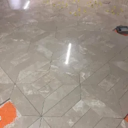 Układanie płytek podłogowych w geometryczny wzór gwiazdy z użyciem poziomujących klipsów, widoczne fragmenty pomarańczowej maty pod płytkami.