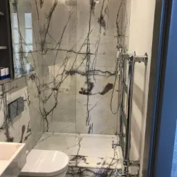 Nowoczesna łazienka z kabiną prysznicową wykończona białym marmurem z czarnymi żyłami, wisząca toaleta i grzejnik drabinkowy w chromowanym wykończeniu.