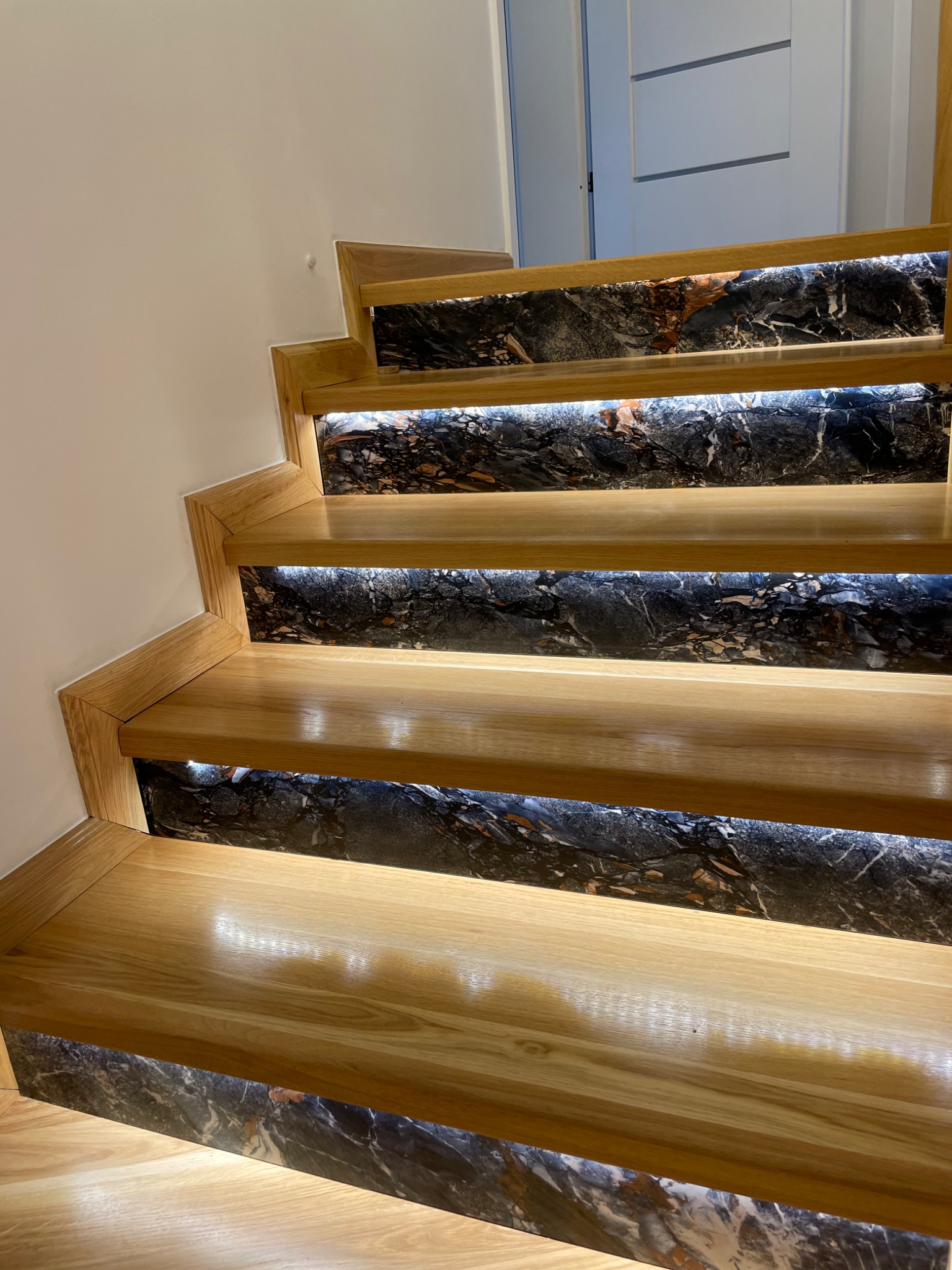 Drewniane schody z marmurowymi podstopnicami i subtelnym podświetleniem LED, widok z dołu, nowoczesny design.