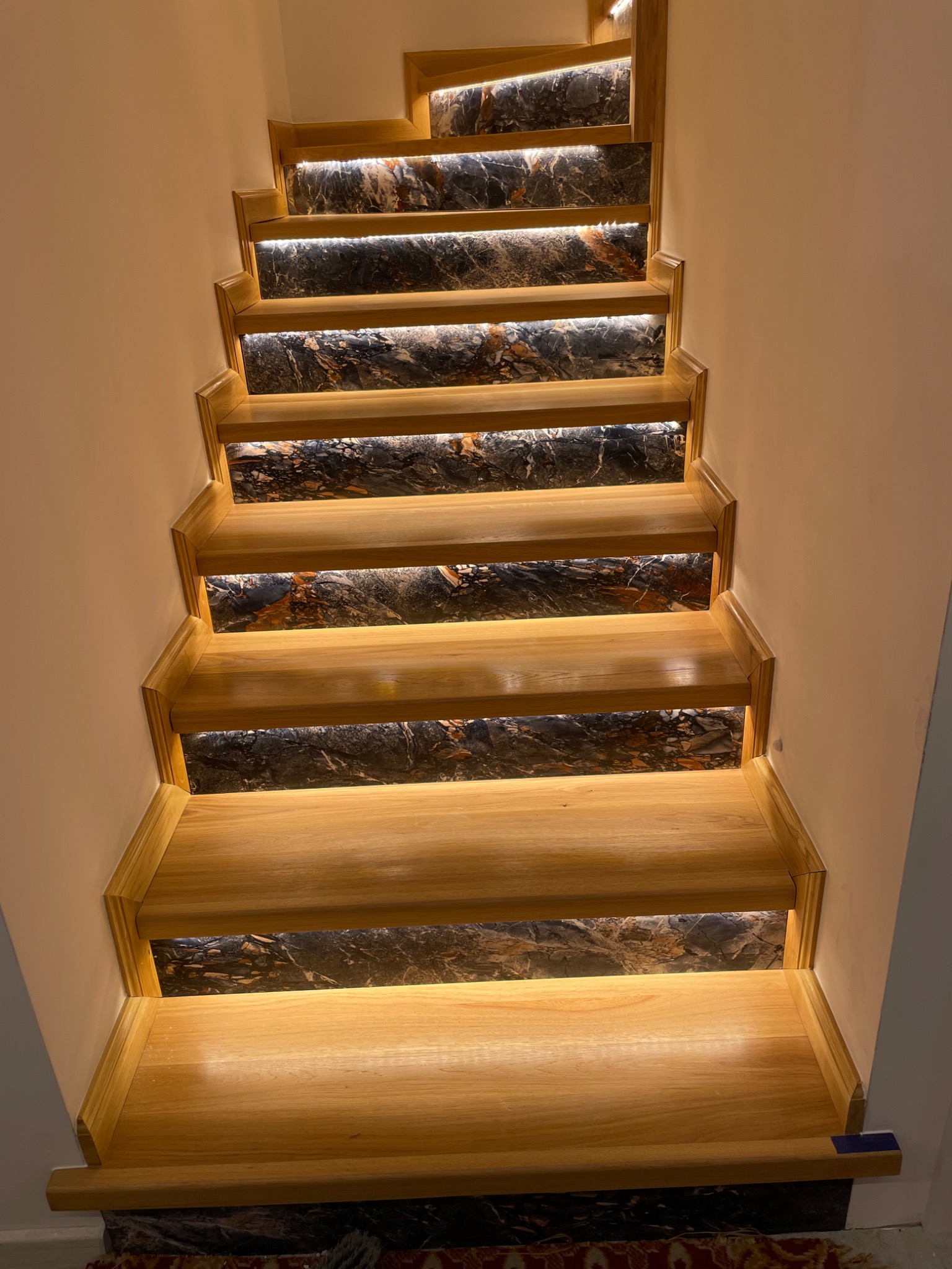 Schody drewniane z podświetlanymi panelami imitującymi marmur, widok z góry, ciepłe oświetlenie.