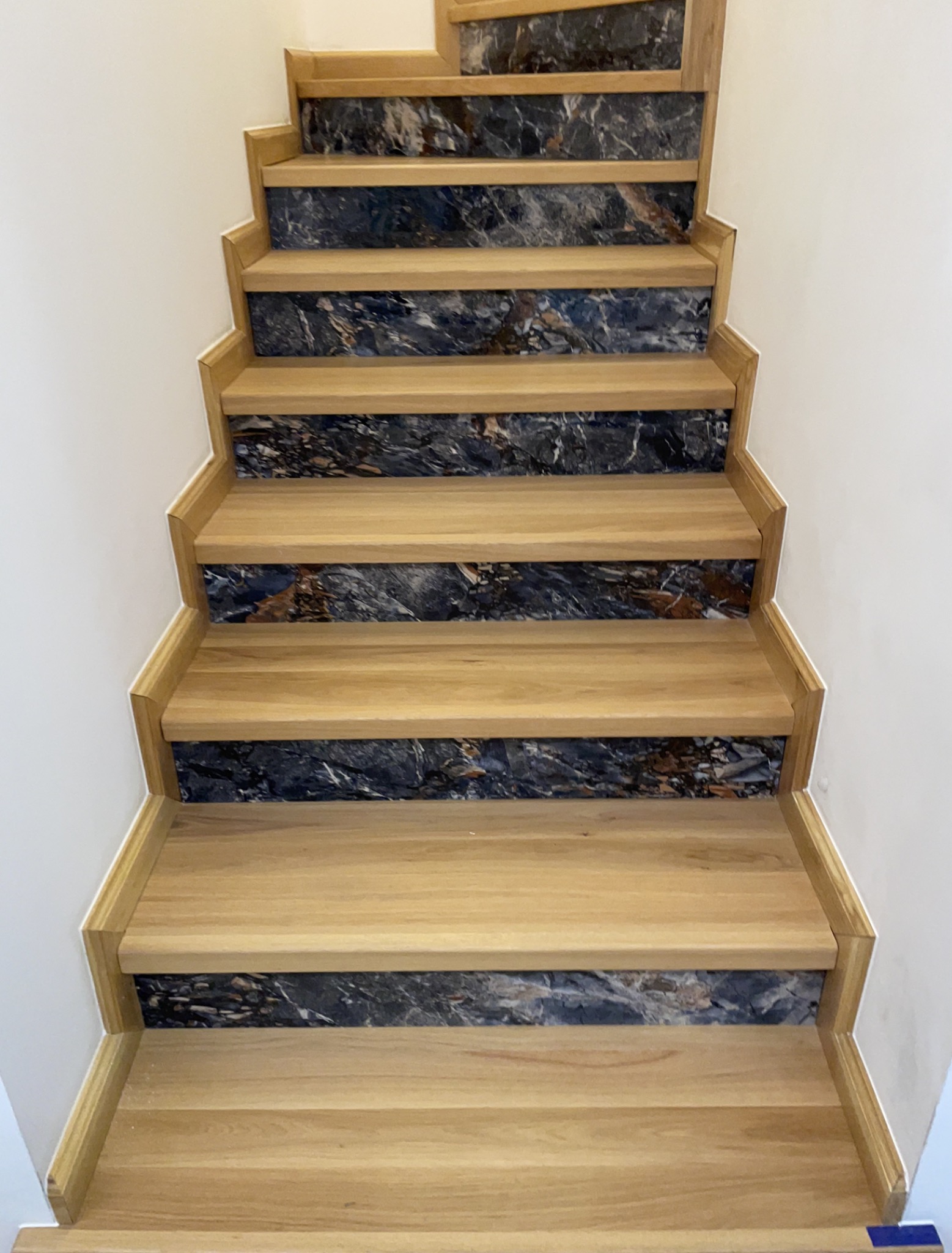 Schody drewniane z wstawkami z ciemnego marmuru, widok z góry, jasne drewno, białe ściany, nowoczesny design.