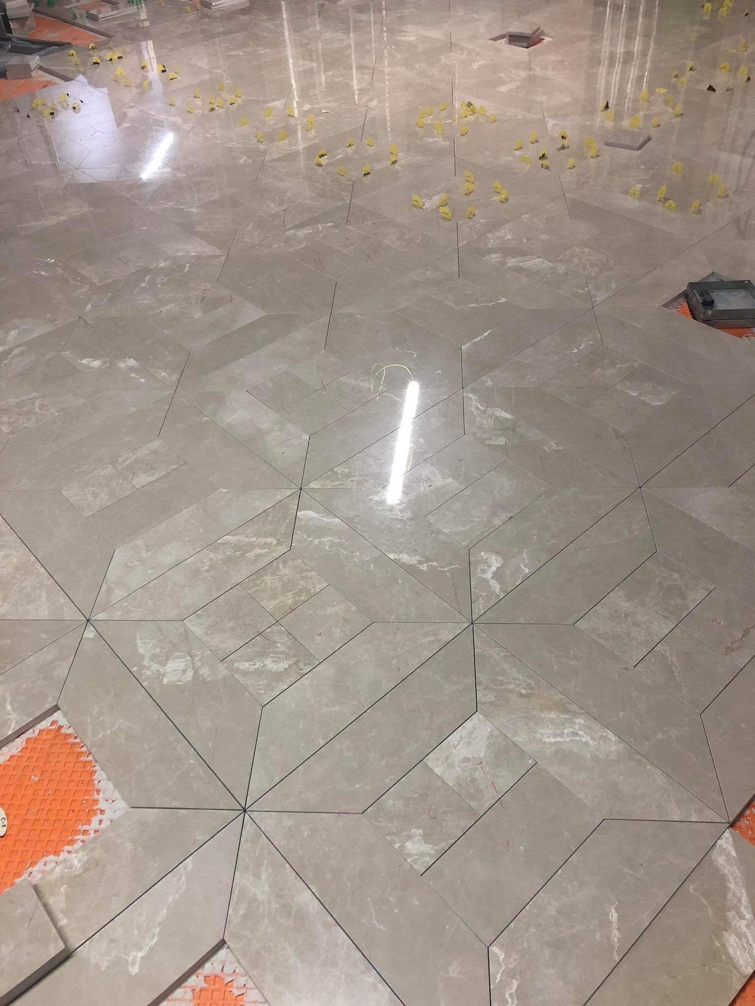 Układanie płytek podłogowych w geometryczny wzór gwiazdy z użyciem poziomujących klipsów, widoczne fragmenty pomarańczowej maty pod płytkami.