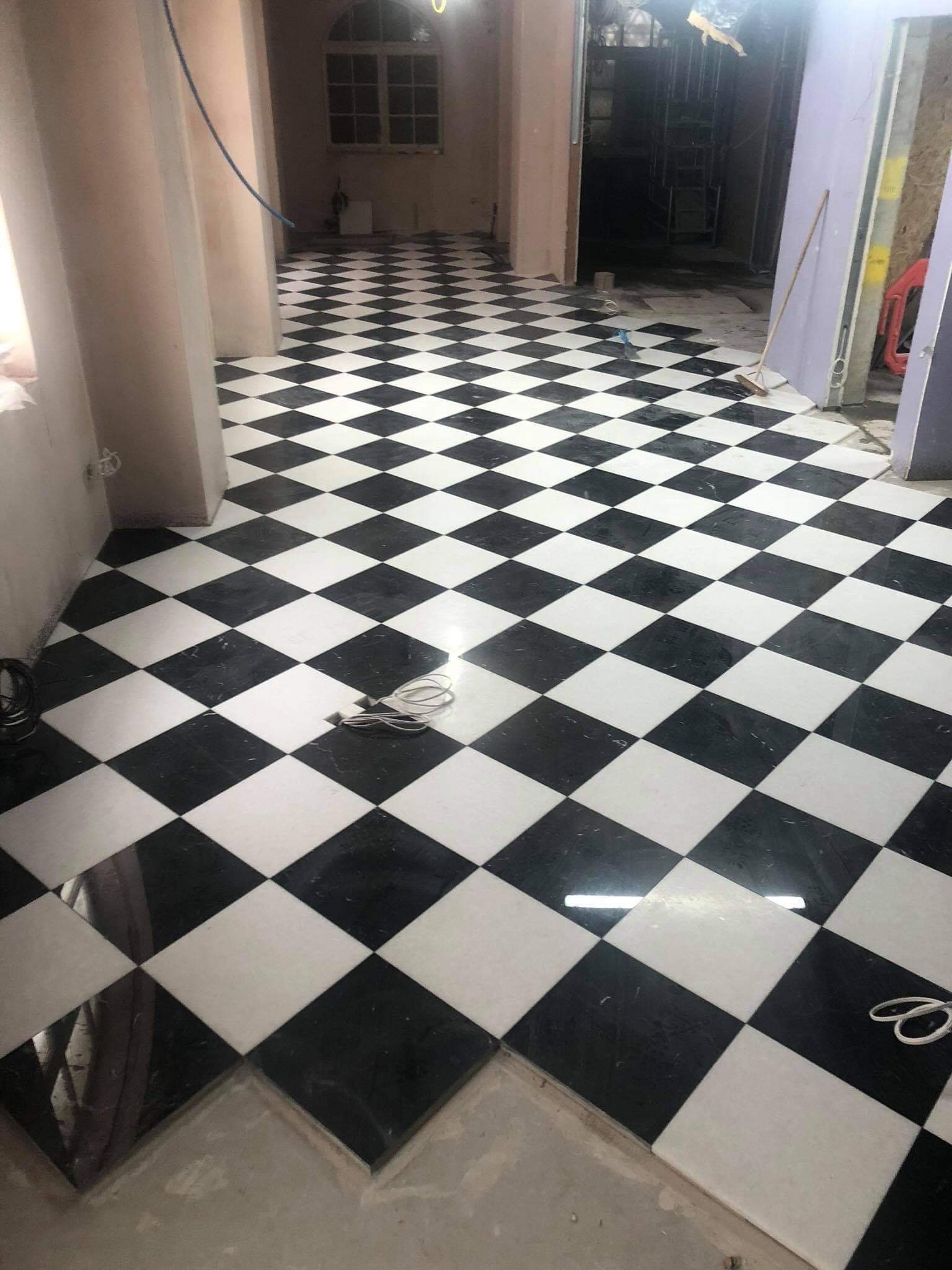 Ułożona pod kątem 45 stopni czarno-biała podłoga w szachownicę z marmuru, widoczna fugą i kable na podłodze, w tle okno z łukiem i rusztowania.