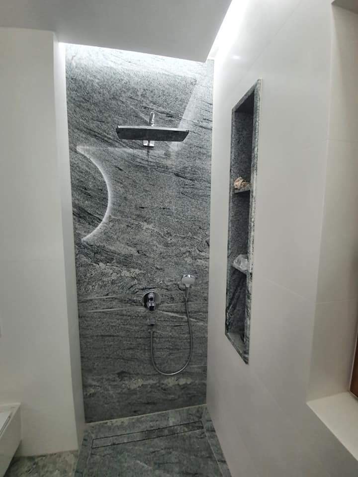 Nowoczesna kabina prysznicowa z szarego kamienia o wyraźnej fakturze, z wnęką w ścianie wykończoną tym samym materiałem, oświetlenie LED w suficie.