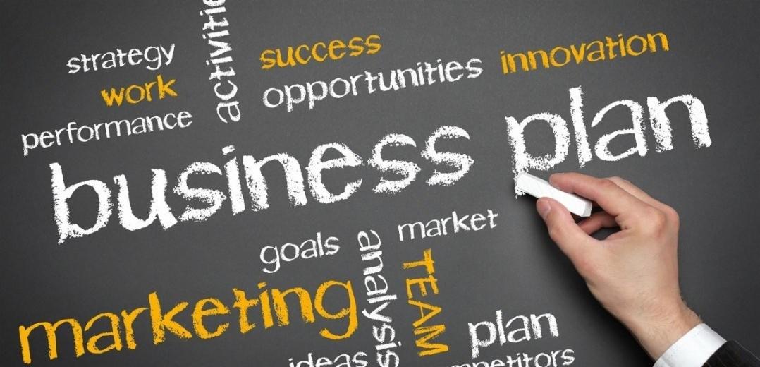 Ręka pisząca kredą na tablicy słowa kluczowe związane ze strategią biznesową, marketingiem i planowaniem.