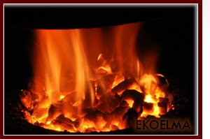 Płonące, rozżarzone bryły paliwa w palenisku, widoczne języki ognia i żarzące się fragmenty, ciemne tło.