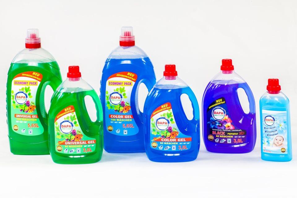 Różnokolorowe butelki z płynem do prania marki DAPA, w tym wersje Universal Gel, Color Gel i Black Renew 3D, ustawione na białym tle.