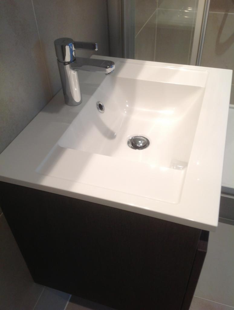 Nowoczesna biała umywalka z chromowaną baterią na szafce z ciemnego drewna, widok z góry, łazienka w szarych tonacjach.