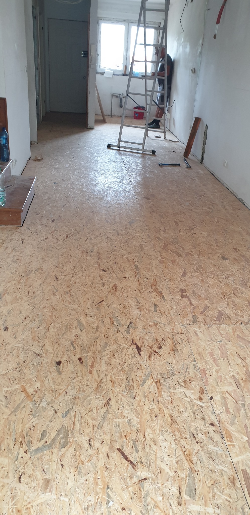 Przygotowanie podłoża z płyt OSB w trakcie remontu mieszkania, widoczna drabina i pracownik przy ścianie.