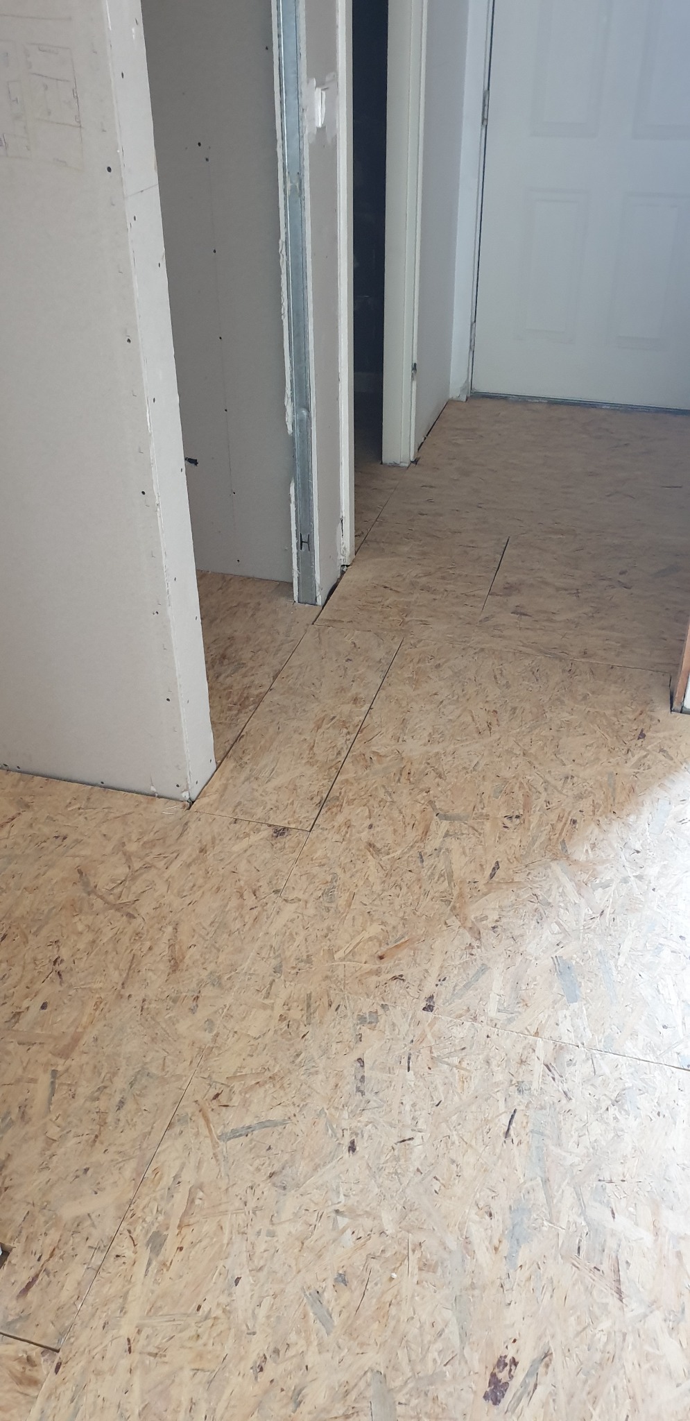 Montaż podłogi z płyt OSB w trakcie remontu, widoczne płyty przycięte do futryn drzwiowych i ścian działowych z elementami metalowej konstrukcji.