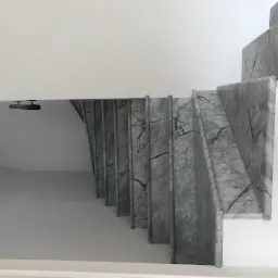 Schody wewnętrzne wykończone szarym marmurem z widocznym rysunkiem żyłkowania, białe ściany i minimalistyczne oświetlenie.