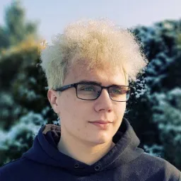 Portret młodego mężczyzny z blond włosami w okularach na tle ośnieżonych drzew.