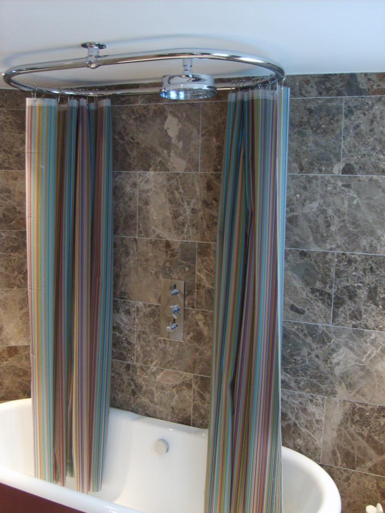 Biała wanna z chromowaną armaturą i prysznicem, zasłonięta kolorową, pionowo prążkowaną zasłoną, na tle ściany wyłożonej marmurowymi płytkami.