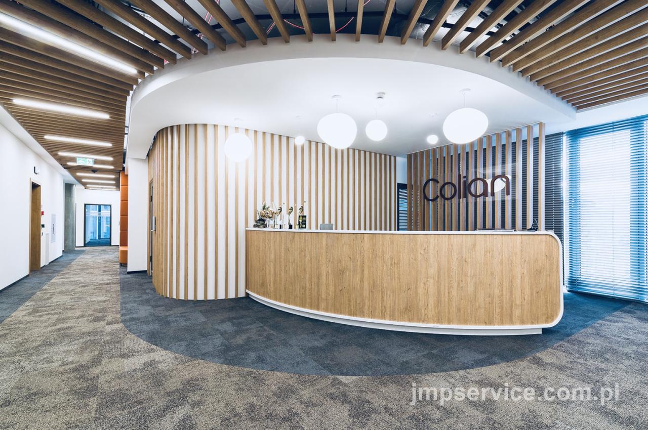 Nowoczesna recepcja biurowa z drewnianą ladą, oświetleniem kulistym i logo firmy Colian na tle pionowych paneli.