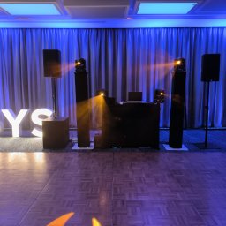 MAR-SOUND - Parkiet taneczny oświetlony reflektorami, w tle kurtyna z niebieskim podświetleniem, kolumny głośnikowe, konsoleta DJ-ska z laptopem i podświetlany napis 'PSYS'.