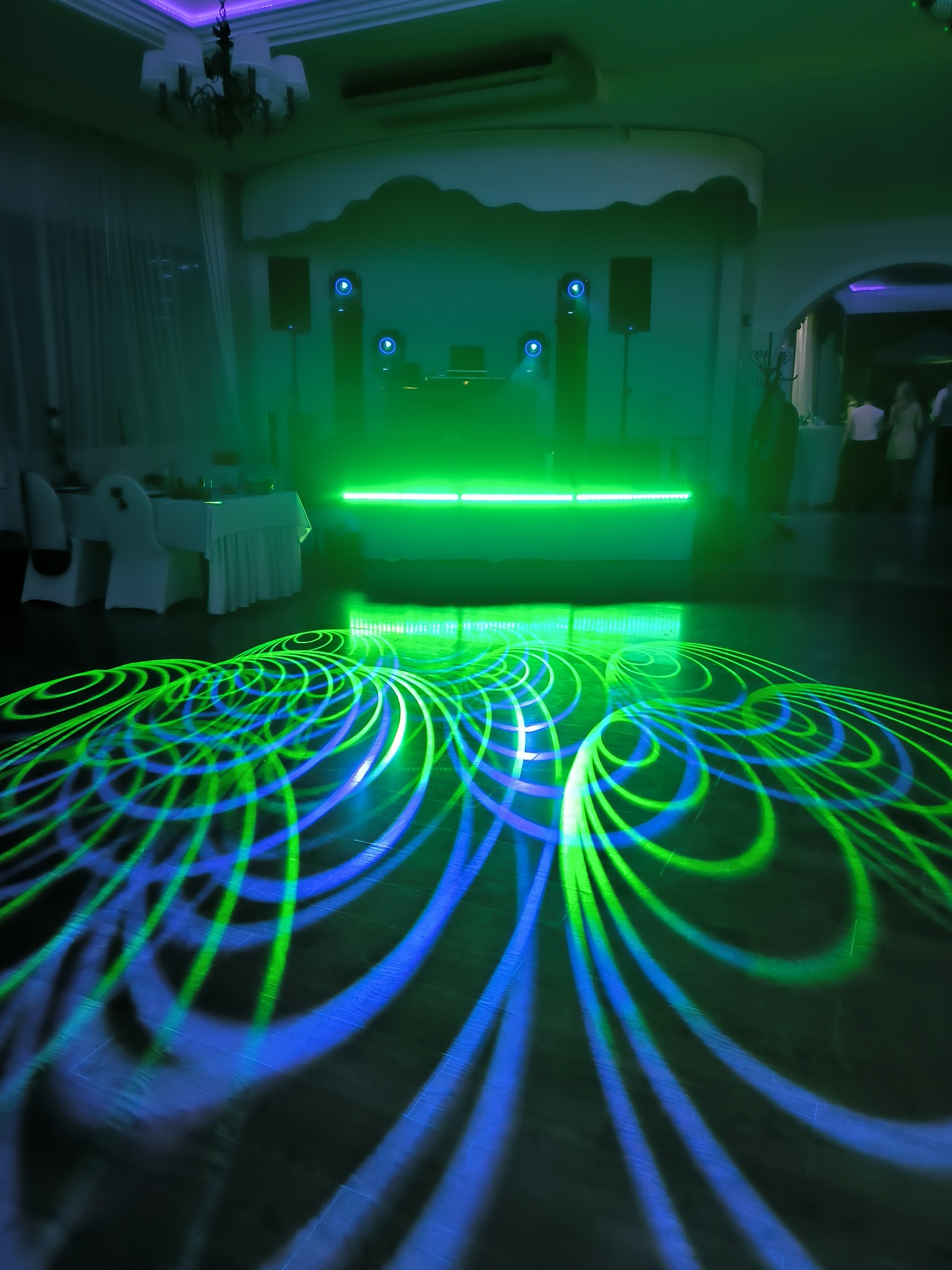 Parkiet taneczny oświetlony wzorami z zielonych i niebieskich laserów, w tle scena z nagłośnieniem i oświetleniem w sali balowej.