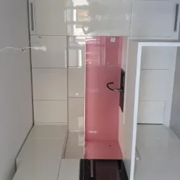 Nowoczesna, biała kuchnia z różowym panelem szklanym nad blatem i minimalistyczną armaturą, oświetlona pojedynczą żarówką na kablu.