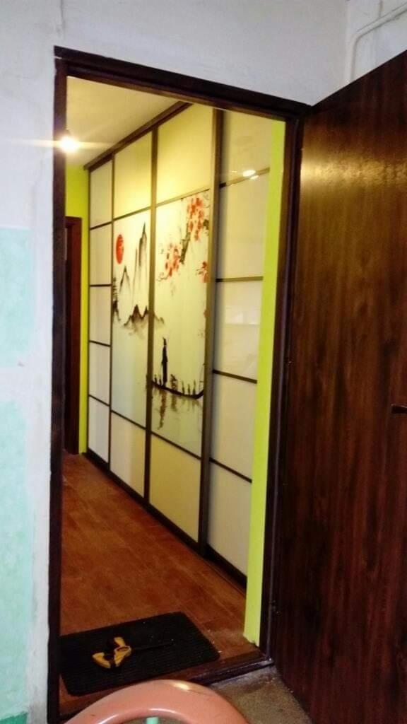 Wnętrze z przesuwnymi drzwiami szafy wnękowej, zdobionymi motywem japońskim z górami, słońcem i sylwetką na łodzi, widoczne z korytarza z drewnianą podłogą i otwartymi drzwiami.