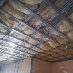 Sufit podwieszany w trakcie montażu z widoczną konstrukcją metalową, ociepleniem z wełny mineralnej i instalacją elektryczną w peszlach