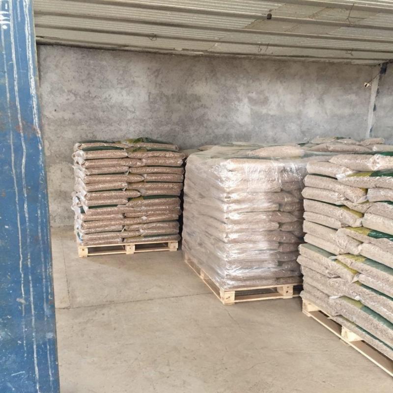 Magazynowane palety z workami pelletu drzewnego, część zafoliowana, na betonowej posadzce pod zadaszeniem.