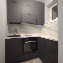 Ciemnoszara zabudowa kuchenna z marmurowym blatem i backsplashiem, widoczny piekarnik z wyświetlaczem, czarny zlew i bateria, oświetlenie podszafkowe.