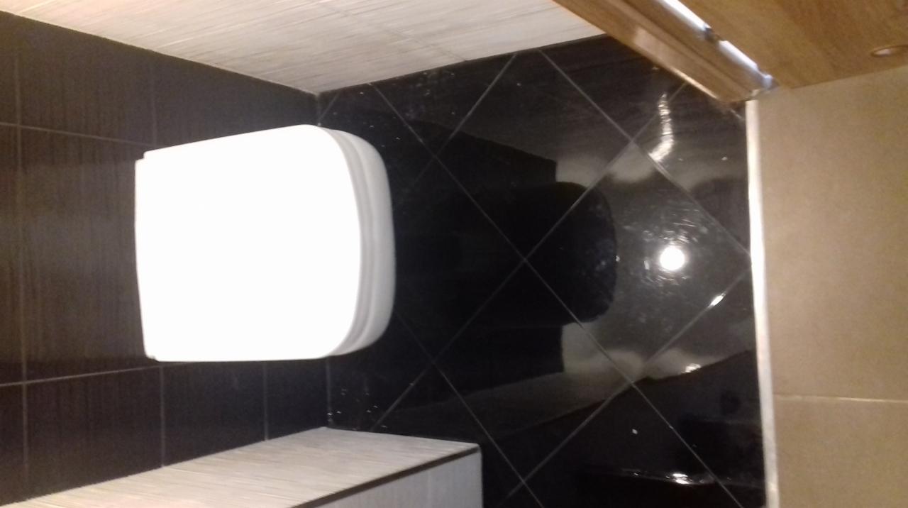 Nowoczesna toaleta wisząca w łazience wykończonej czarnymi, błyszczącymi płytkami ułożonymi w karo, z blatem z jasnego marmuru.