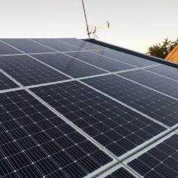 Instalacja paneli słonecznych na dachu domu jednorodzinnego, widoczna antena telewizyjna w tle.