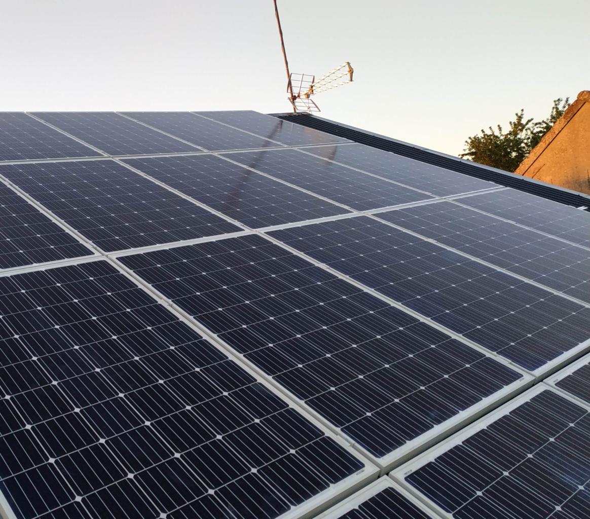 Instalacja paneli słonecznych na dachu domu jednorodzinnego, widoczna antena telewizyjna w tle.