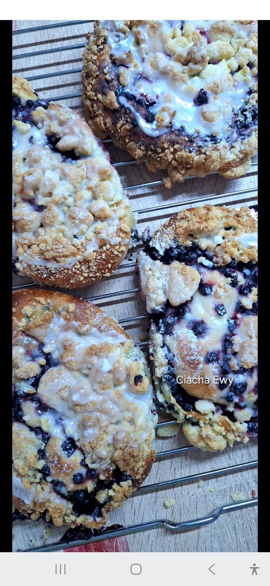 Domowe jagodzianki z kruszonką i lukrem na metalowej kratce, uchwycone z bliska pod kątem. W tle widoczny blat stołu.