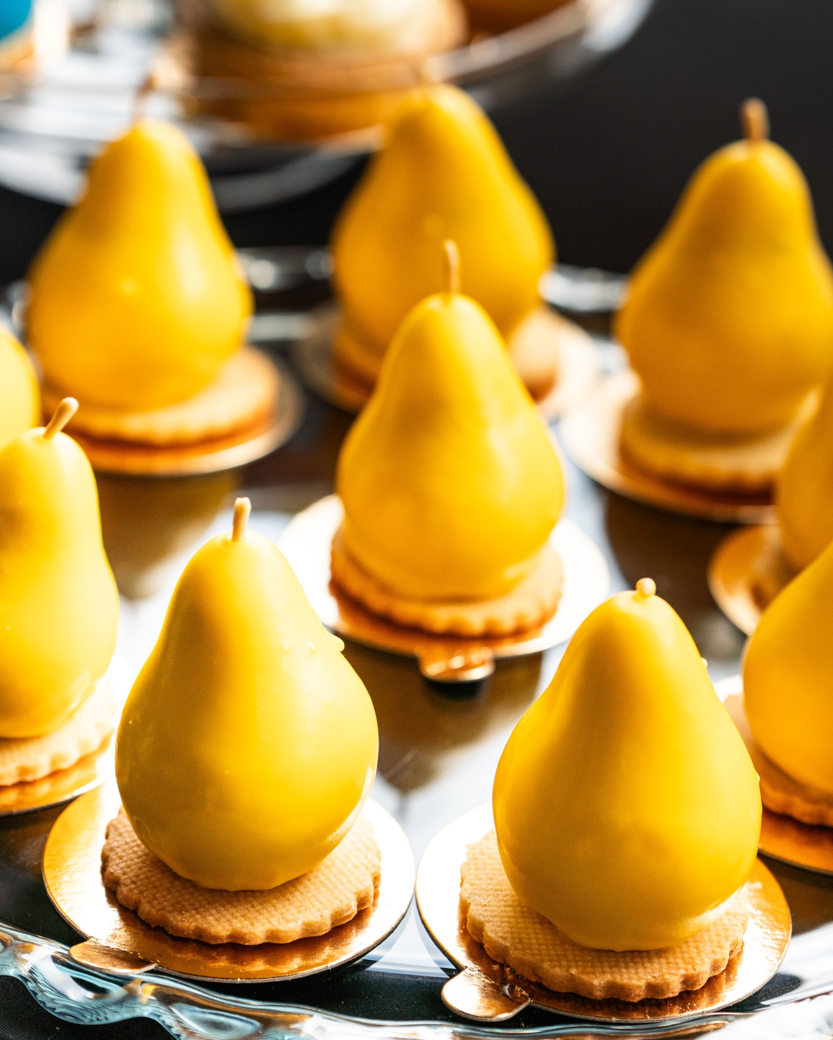 Żółte desery w kształcie gruszek na kruchym spodzie, elegancko ułożone na srebrnej tacy. Słodki poczęstunek na przyjęciu.