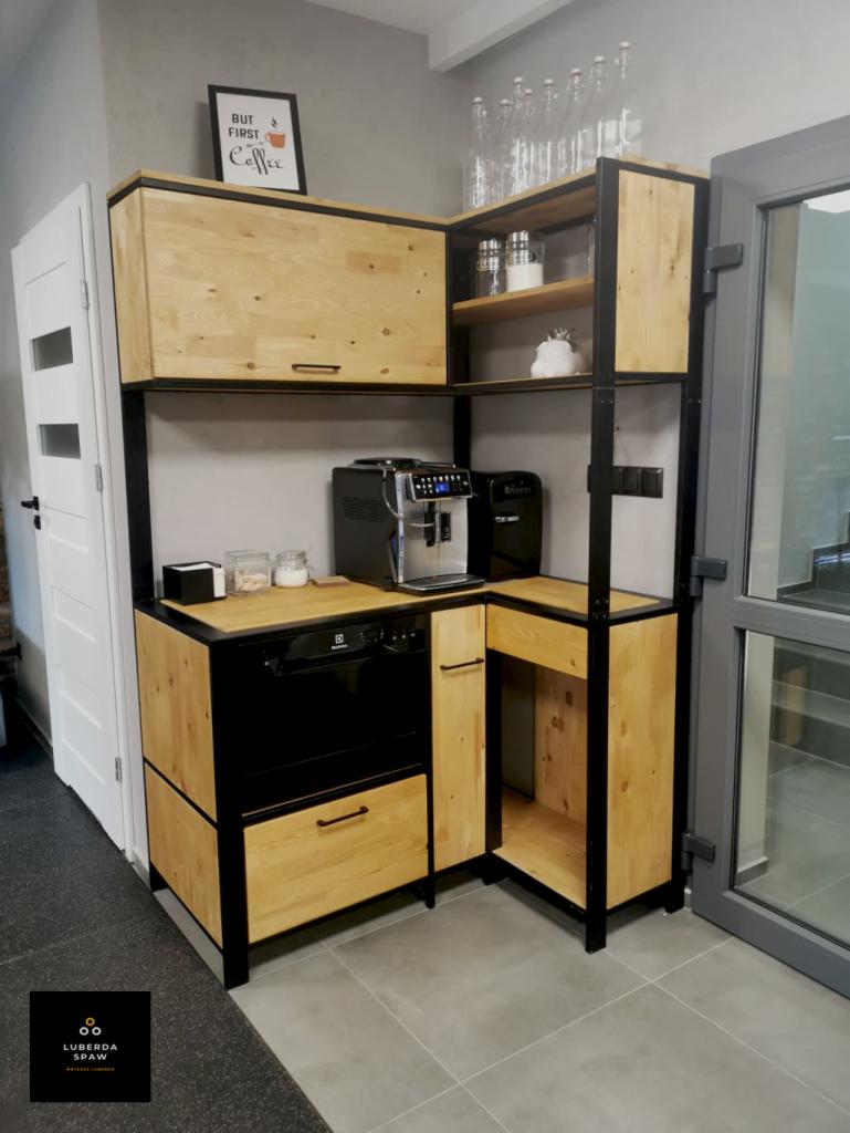 Kuchenna zabudowa narożna z jasnego drewna i czarnych metalowych ram, z wbudowaną zmywarką i ekspresem do kawy, uzupełniona dekoracyjnymi butelkami na półce i plakatem 'But first coffee'.