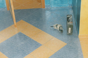 Ułożona, kwadratowa podłoga z płytek w kolorach niebieskim i beżowym, widoczne narzędzia pracy glazurniczej: wiertarka i poziomica.