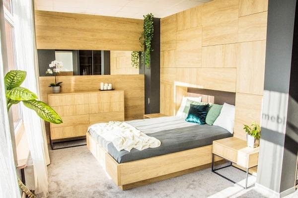 Komplet mebli do sypialni na wymiar: łóżko z drewnianą ramą, szafka nocna z metalowymi nogami, komoda z minimalistycznymi uchwytami, drewniana ściana z wbudowanym lustrem i zieloną rośliną pnącą.