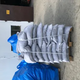 Ułożone na palecie worki z czarnym granulatem, zabezpieczone sznurkiem, widoczne na tle betonowej kostki brukowej i ściany budynku z żółtą tabliczką informacyjną.