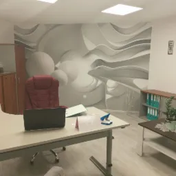 Wnętrze biura z nowoczesną tapetą 3D, biurkiem z laptopem, czerwonym fotelem i regałem z segregatorami.