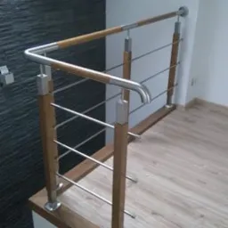 Nowoczesna balustrada schodowa z drewnianymi słupkami i metalowymi prętami, zamontowana w domu w Piotrkowie Trybunalskim, widok z góry na schody z drewnianymi stopniami i fragmentem szarej ściany...