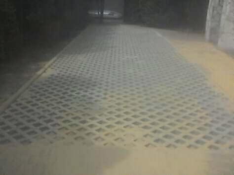 Szara ażurowa nawierzchnia ułożona na posesji, wypełniona piaskiem, widoczna w słabym oświetleniu.