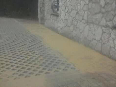 Umyta kostka ażurowa przylegająca do kamiennej ściany budynku, widoczne ślady piasku na powierzchni.