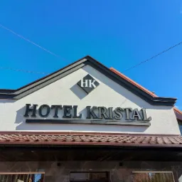 Elewacja hotelu z czarnym napisem 'HOTEL KRISTAL' i logo HK w rombie, na tle błękitnego nieba.
